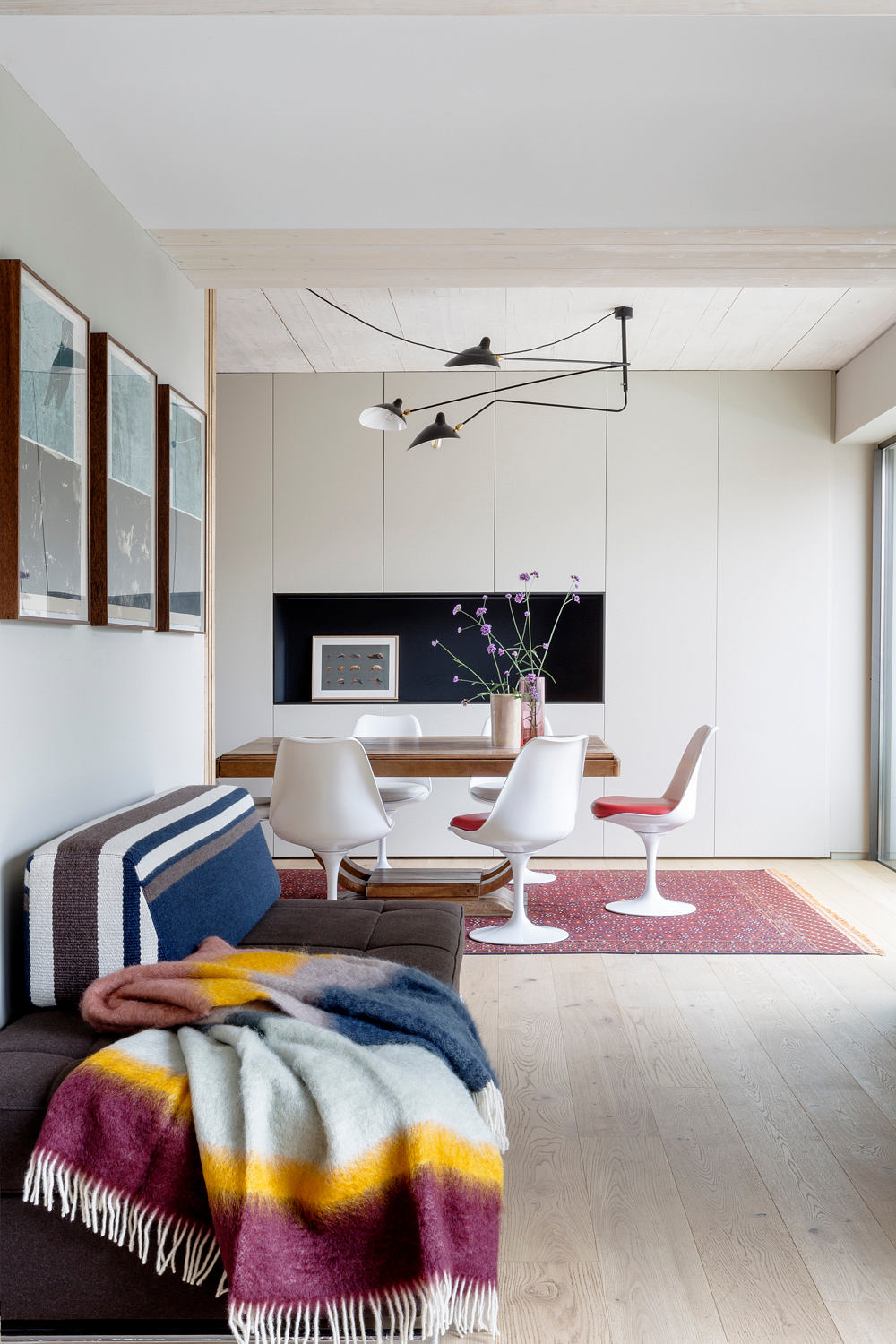 Modern living room with white chairs, wooden floor, and a colorful blanket.