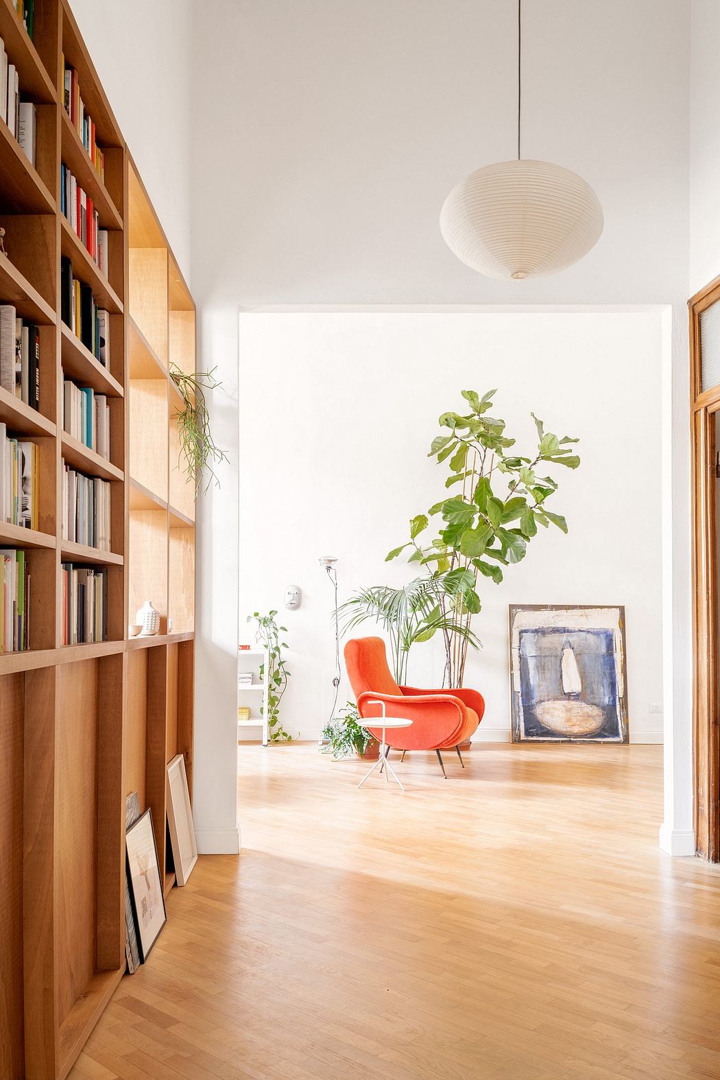 Bright room with bookshelf, wooden floors, and a red chair.