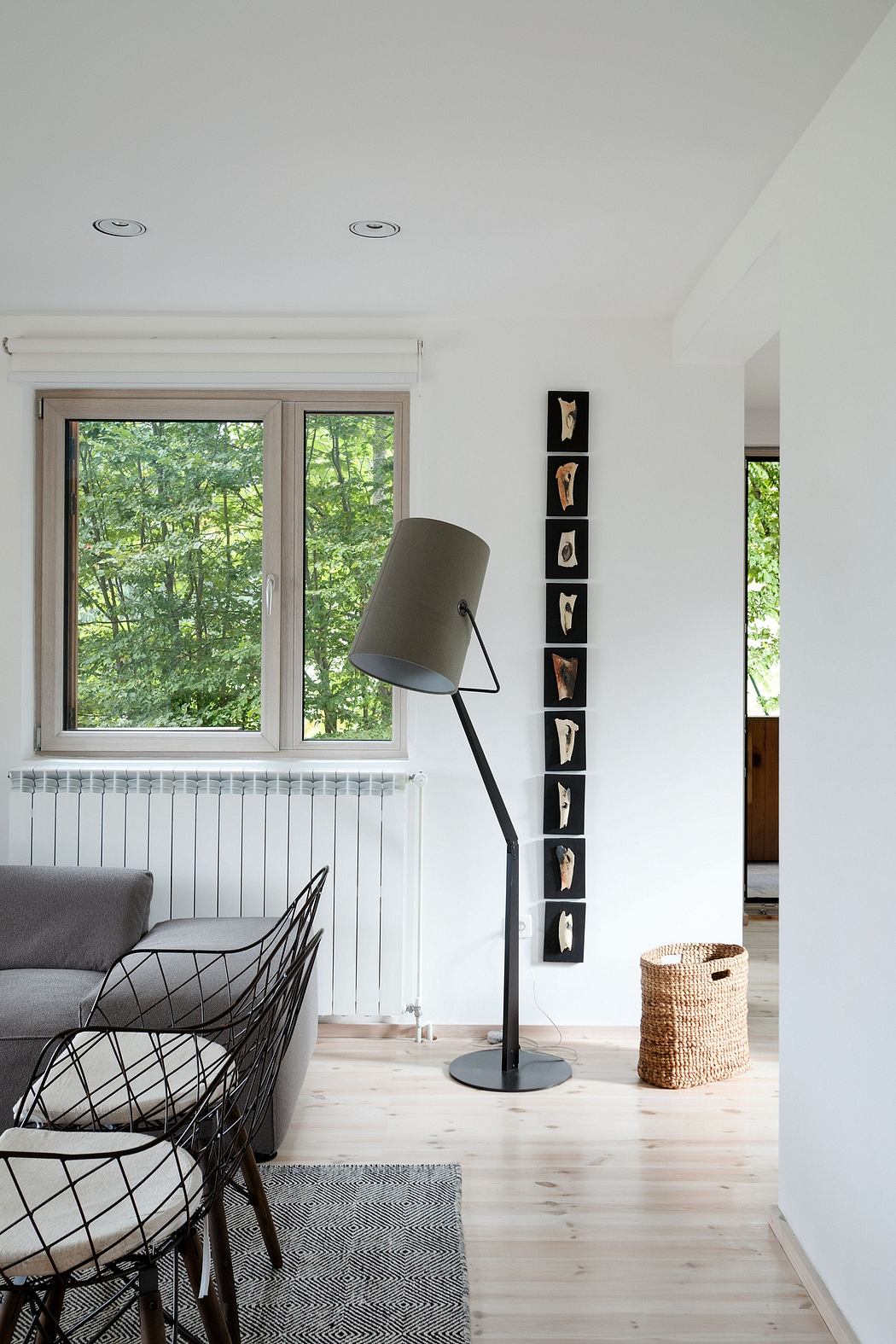 Minimalist living room with large windows overlooking lush greenery, modern lamp, and framed artwork.