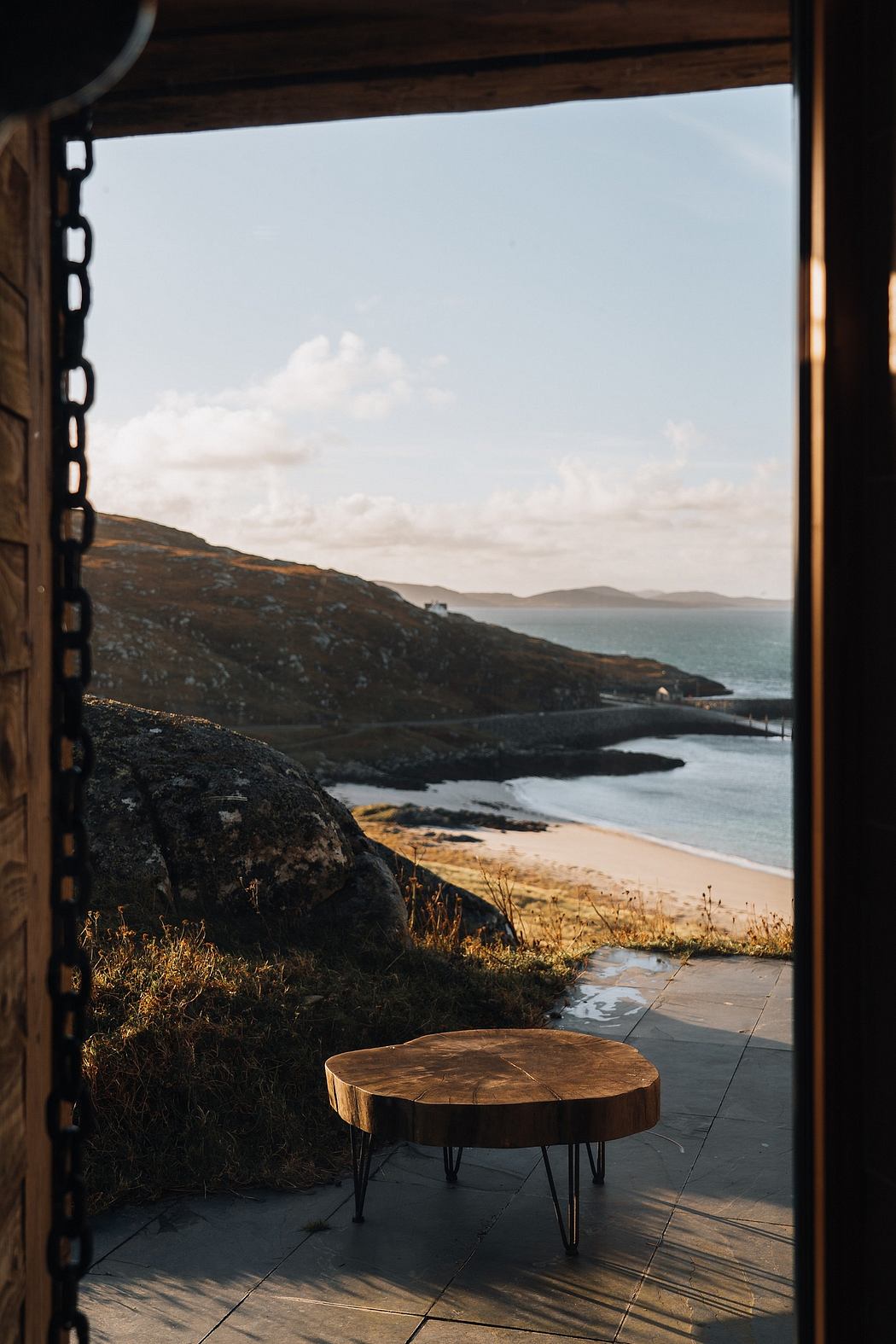 View of a beach and hills through an open door with a wooden table in the
