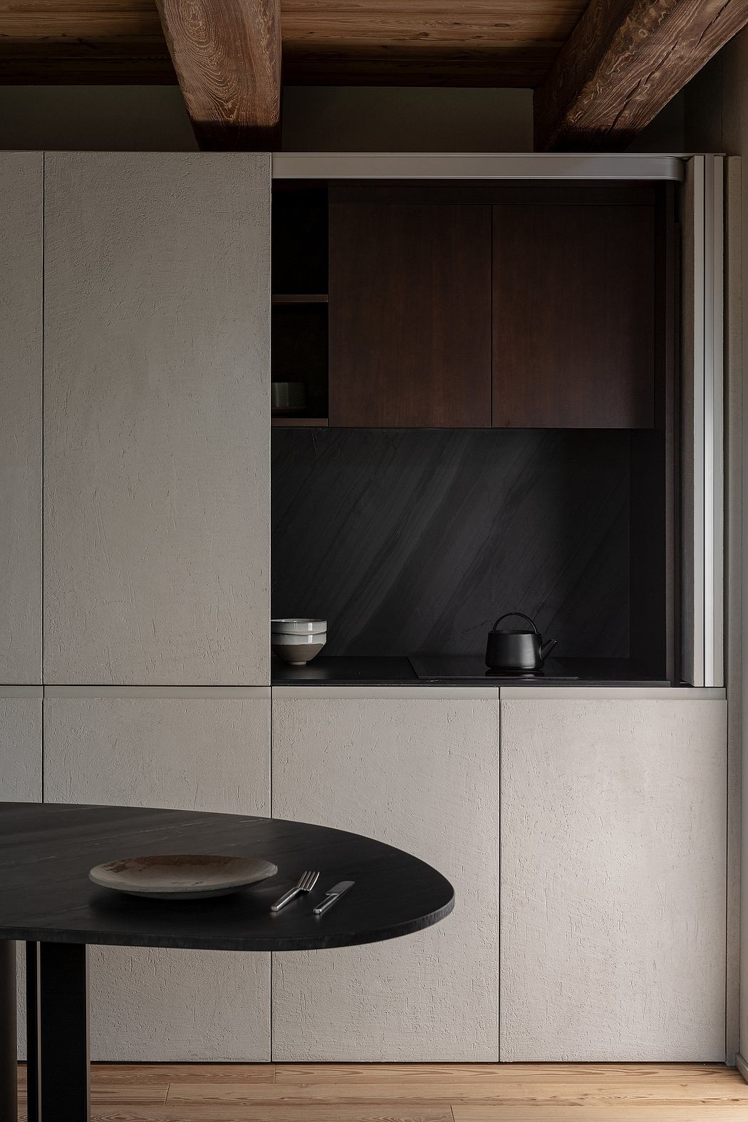 Modern kitchen corner with wooden beams, black table, and minimalist cabinetry.