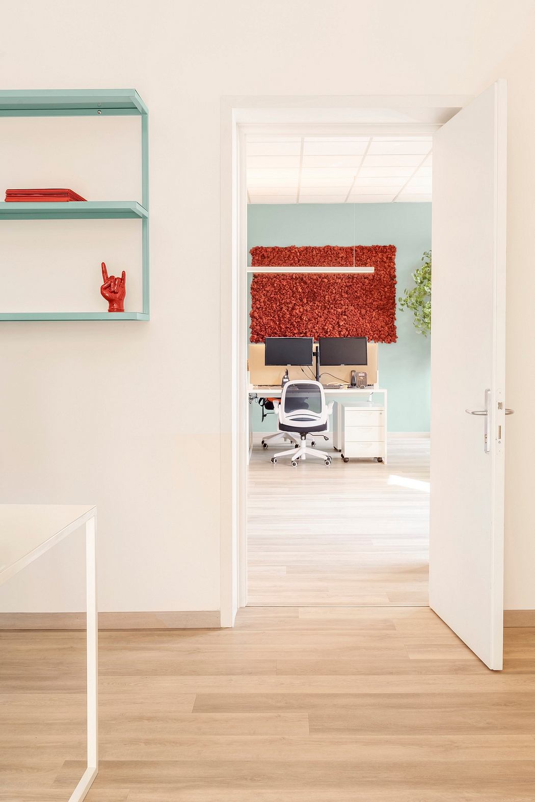Modern office space with minimalist shelving, red textured wall, and ergonomic desk setup.