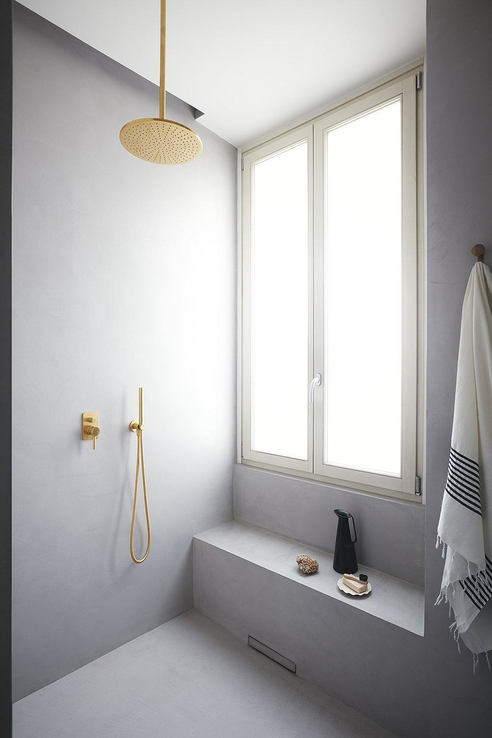 A minimalist bathroom design featuring a gold shower head and fittings, white walls, and a large window.