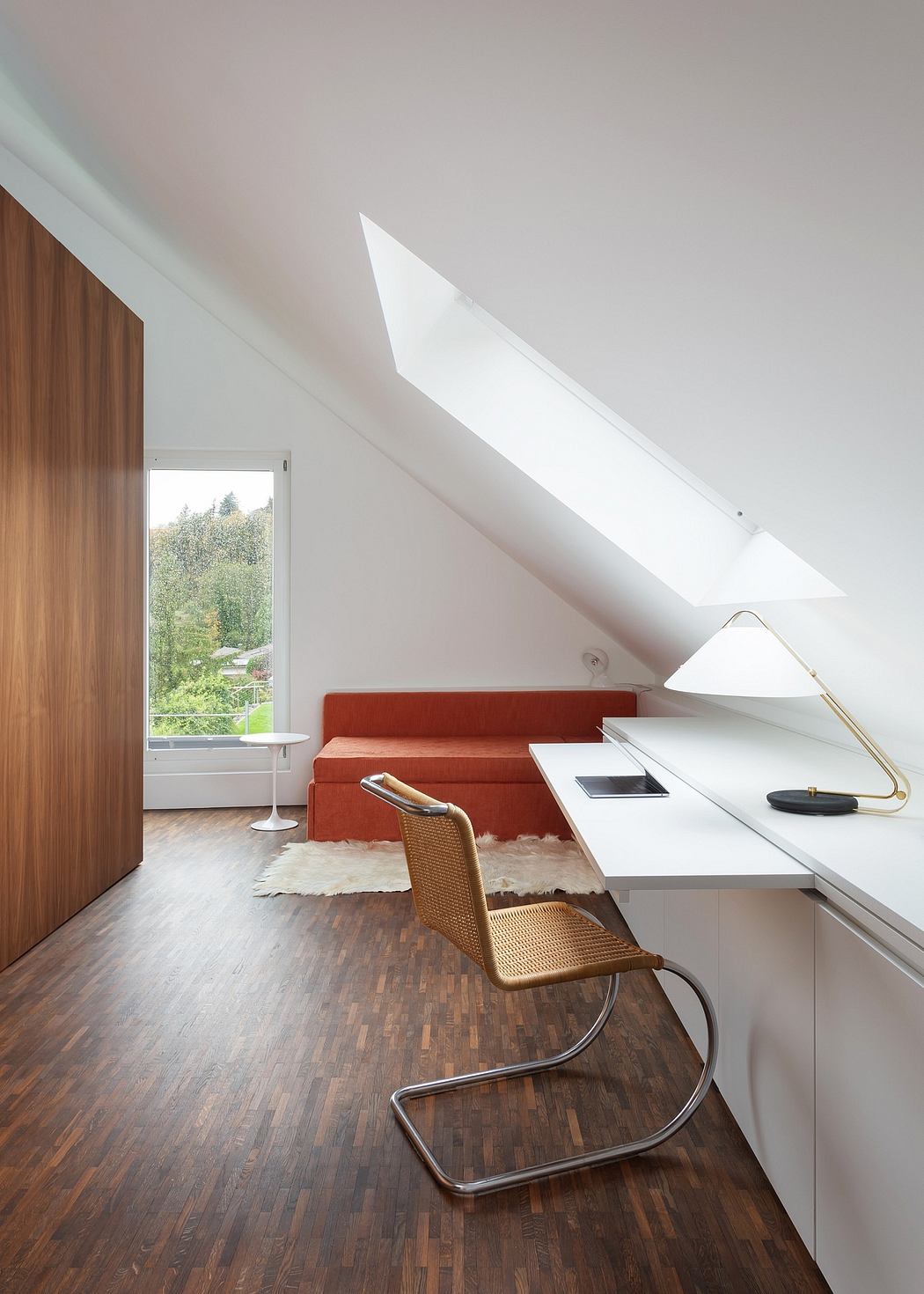 Modern loft-style room with wooden floors, white walls, and a large window offering a view.