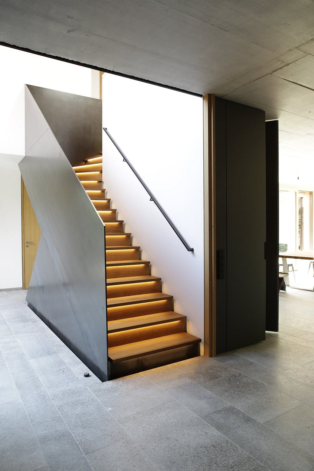 Modern staircase with illuminated wooden steps and a metal handrail.