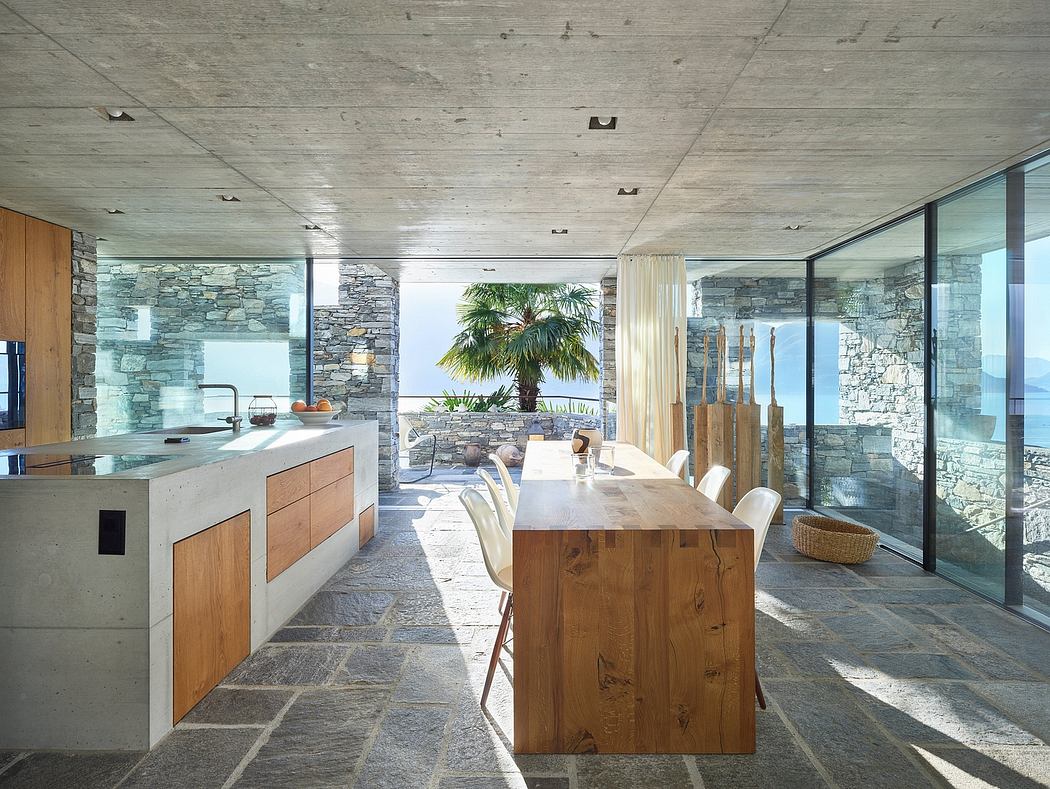 Contemporary open-plan kitchen with ocean view, wooden table, and stone walls.
