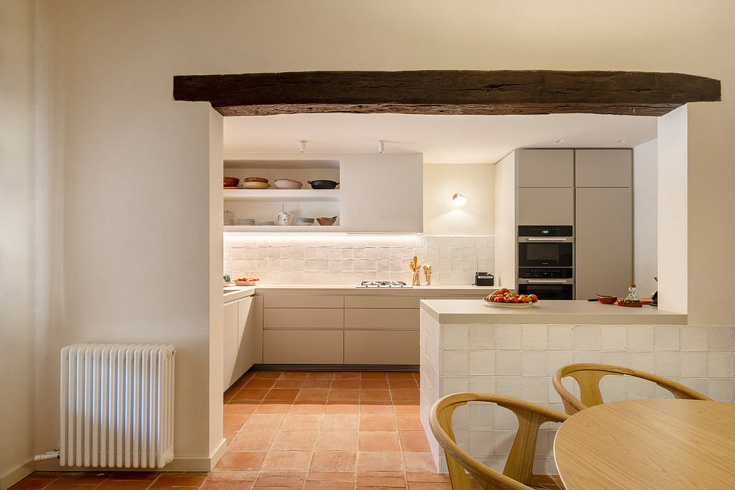 A modern kitchen with white cabinets, wooden beams, and terracotta tile flooring.
