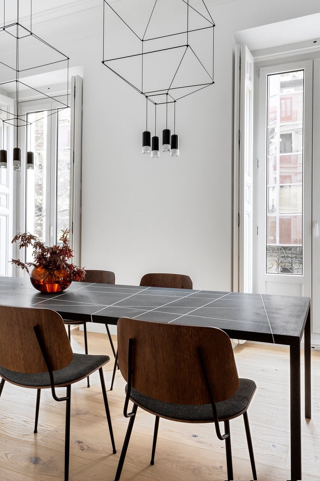 Modern dining room with geometric ceiling lighting, tiled table, and wooden chairs.