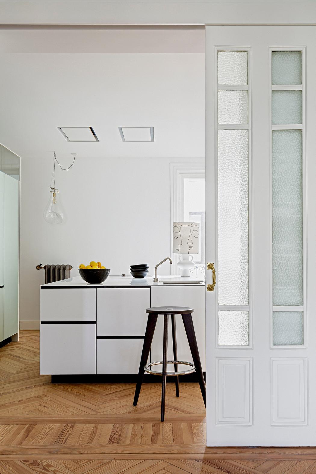 Minimalist kitchen with herringbone floor and white cabinetry.