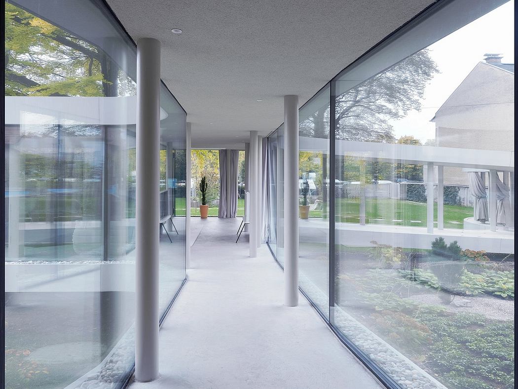 Spacious glass-enclosed corridor with minimalist columns and views of the garden.