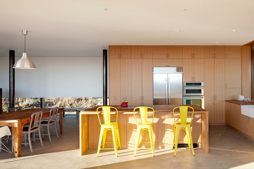 Modern kitchen with wooden cabinets and yellow chairs.
