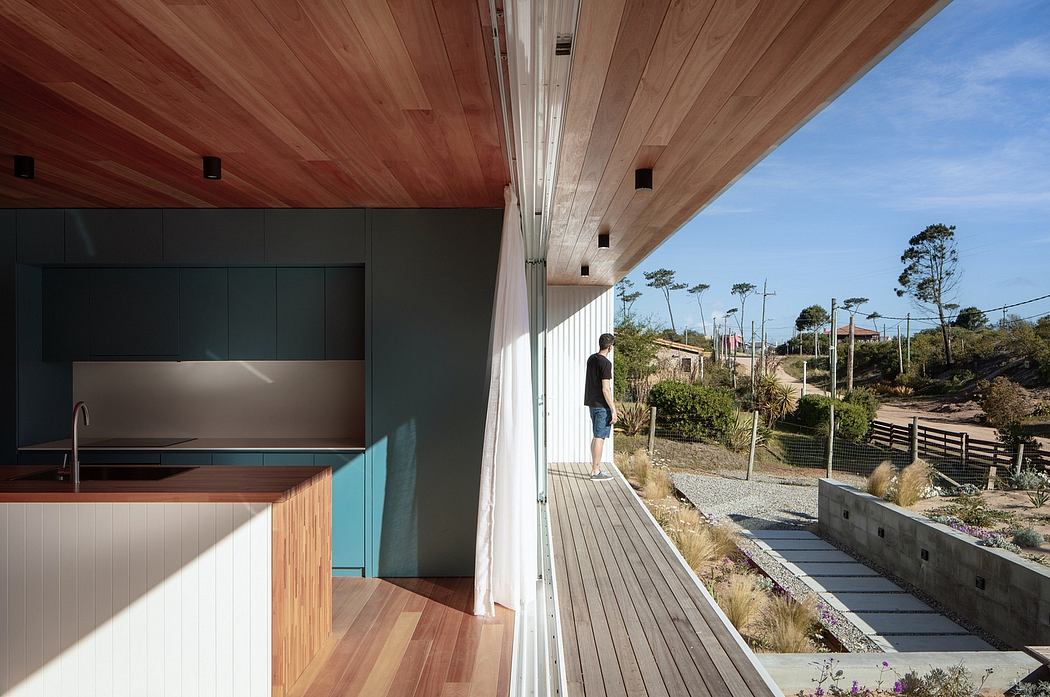 A modern kitchen with wooden ceiling and a person standing on the outdoor deck.