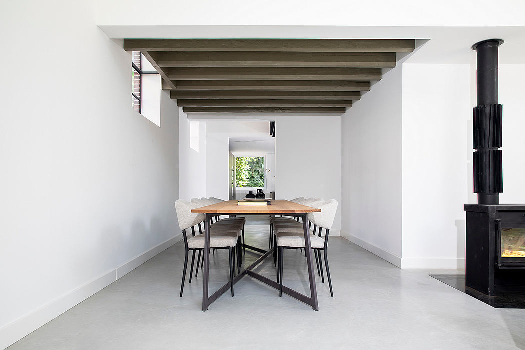 An airy, minimalist dining room with exposed wooden beams, a modern table, and a fireplace.