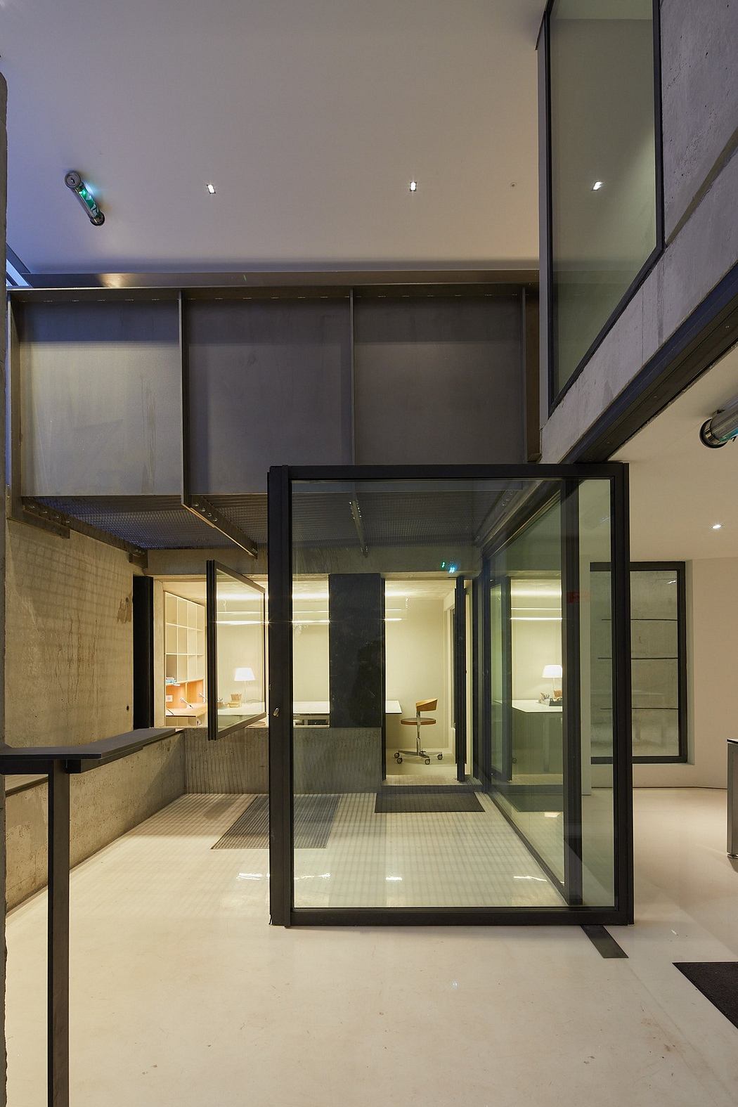 A modern, minimalist interior with glass partitions, shelves, and recessed lighting.