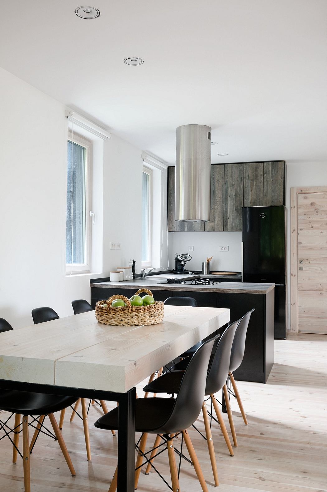 A modern kitchen with a wooden feature wall, black cabinets, and a large dining table.
