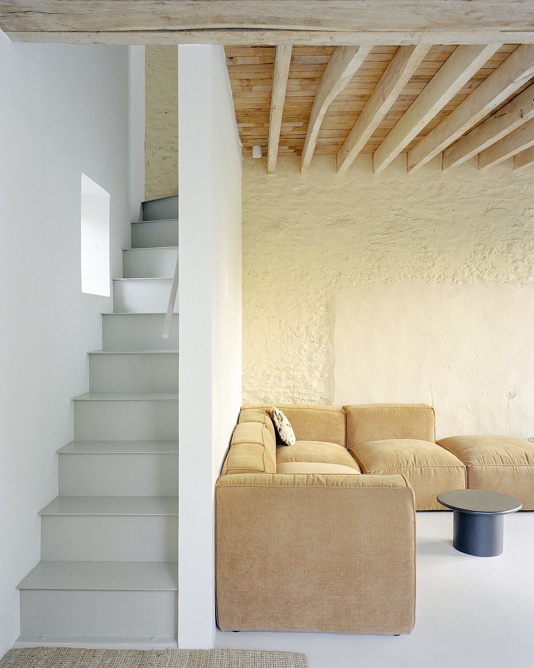 Minimalist stairway beside a tan couch under a wooden beam ceiling.