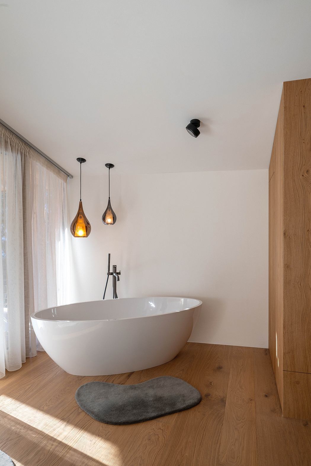 Modern bathroom with freestanding tub, wood-paneled accents, and pendant lighting.