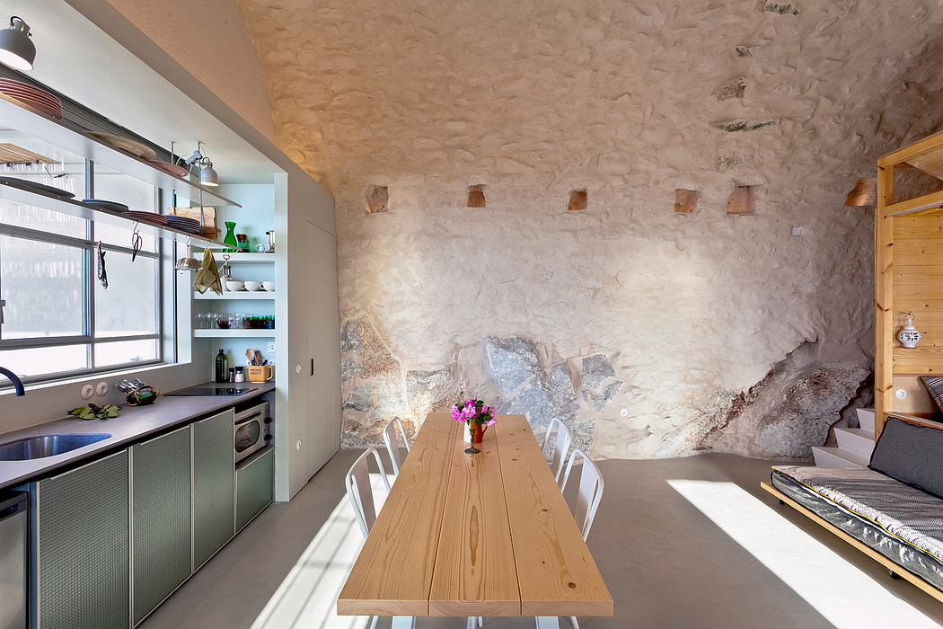 A rustic kitchen with exposed stone walls, wooden dining table, and modern appliances.