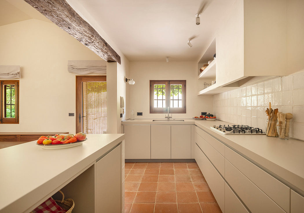 Cozy kitchen with wooden beams, neutral tones, and terracotta tile flooring.
