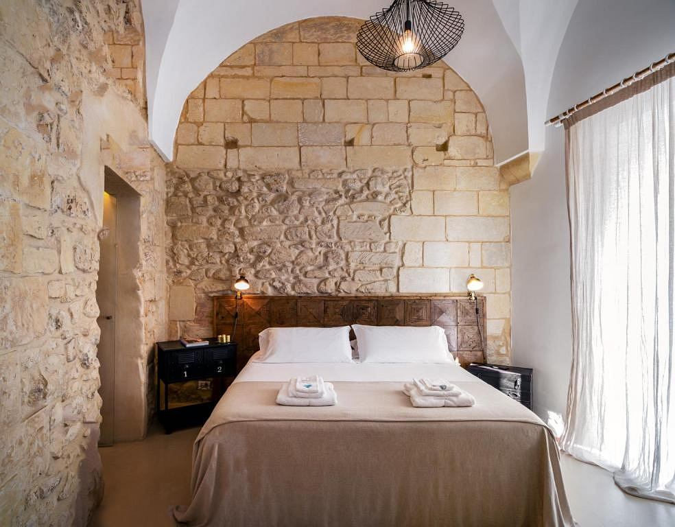 A cozy bedroom with a vaulted stone ceiling, wooden furniture, and a modern light fixture.