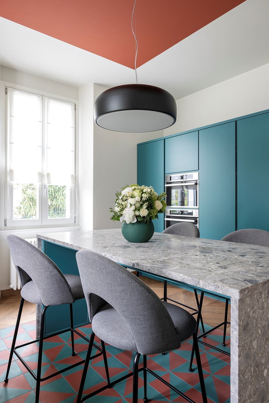 Sleek modern kitchen with bold teal cabinets, marble countertop, and stylish pendant light.