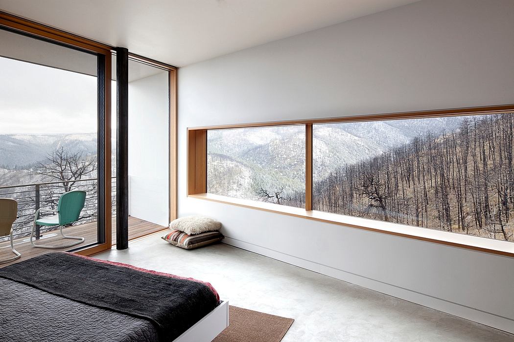 Minimalist bedroom with large windows overlooking snowy mountains.