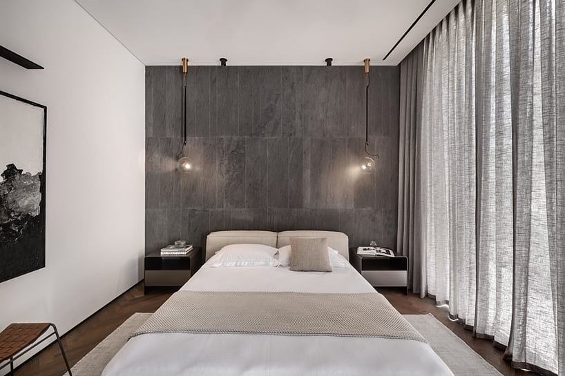 A modern, minimalist bedroom with a large gray marble wall, pendant lights, and gray curtains.
