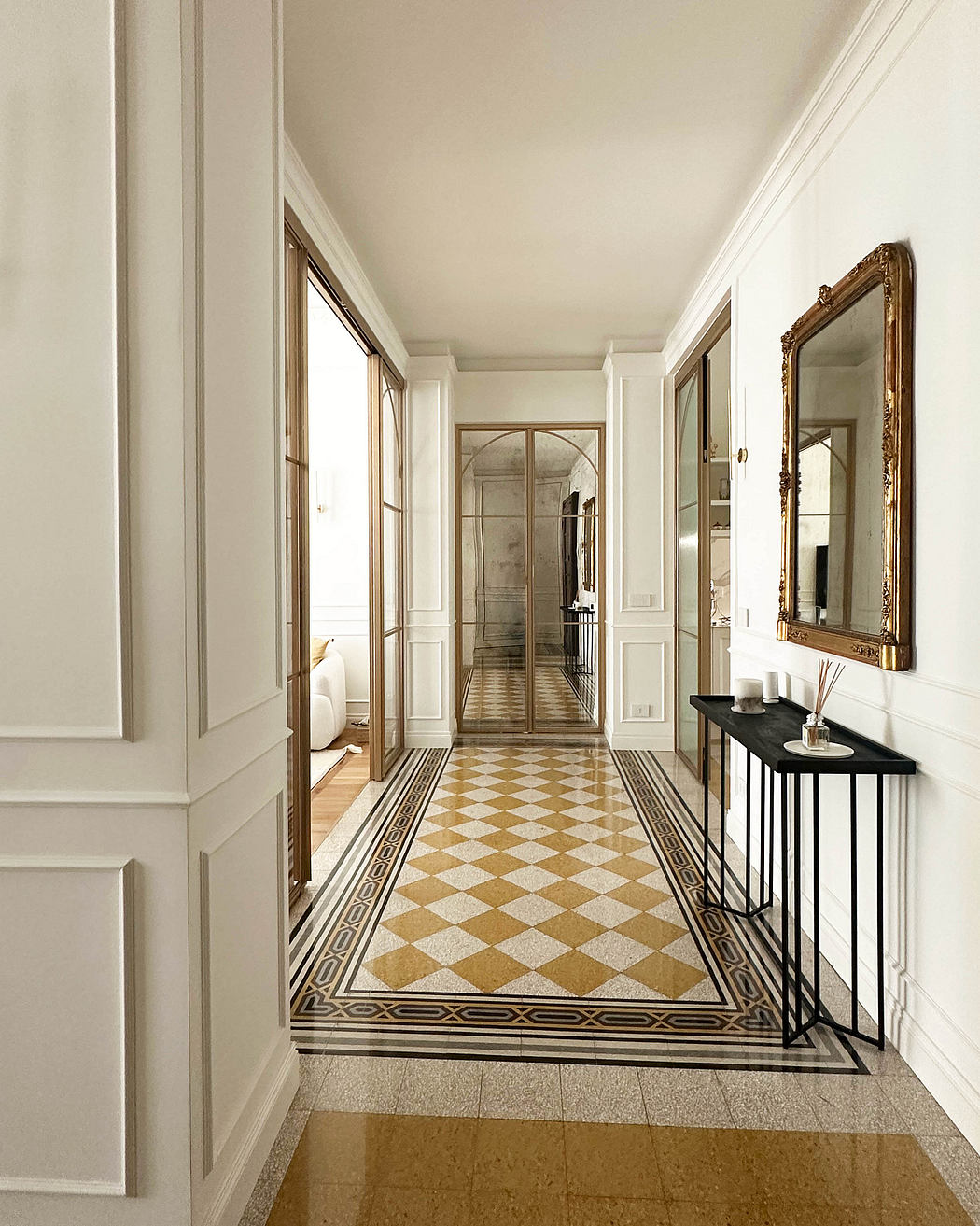 Elegant hallway with checkered floor, white walls, and decorative mirror.