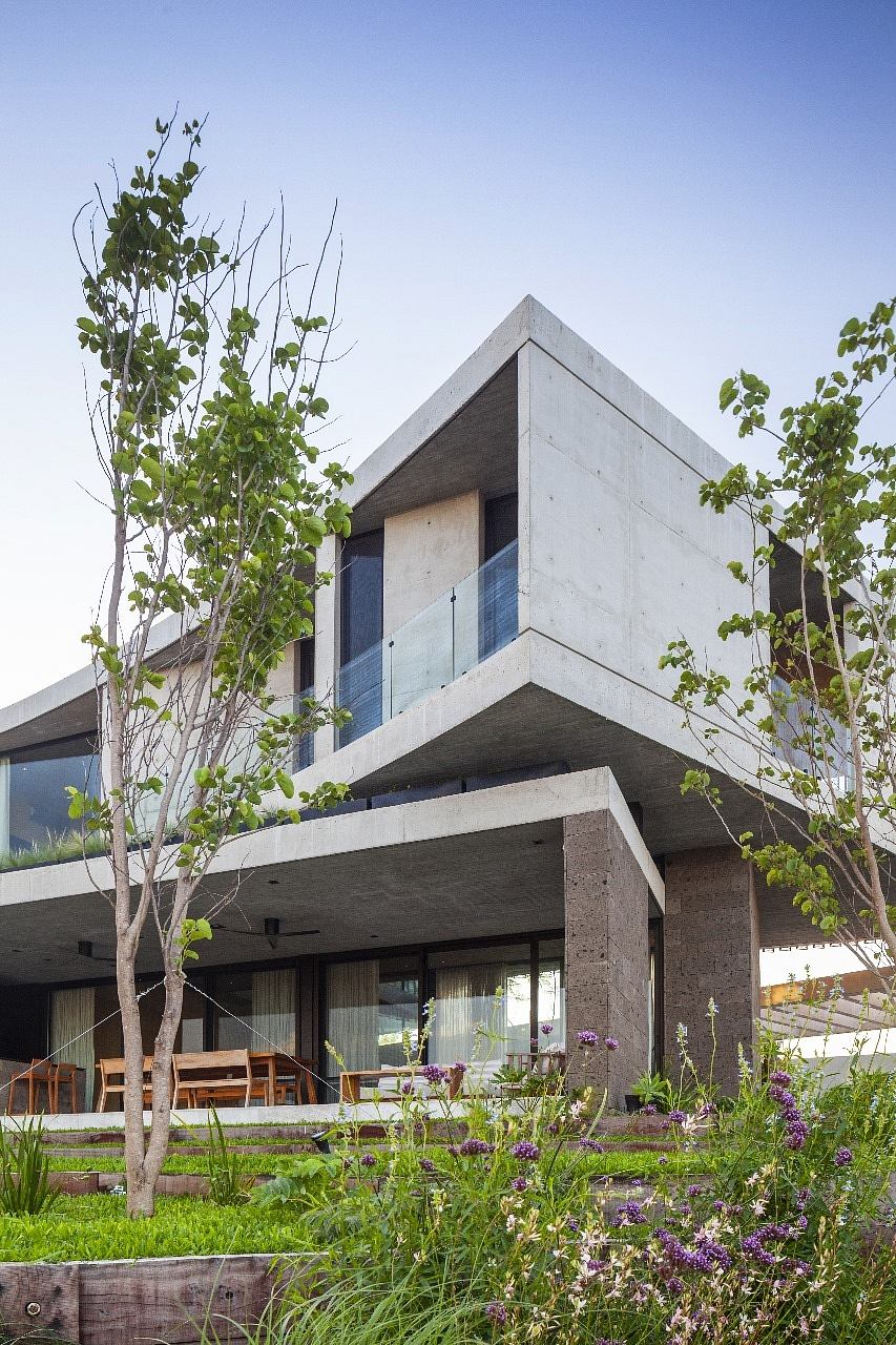 Angular concrete home with large glass windows, surrounded by greenery.