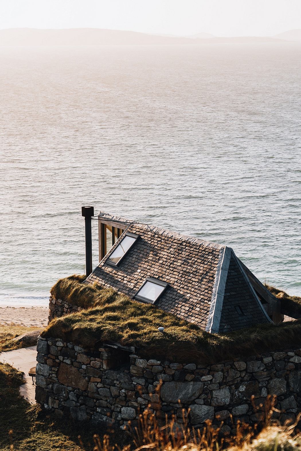 Seaside cabin with grass roof blending into coastal landscape.