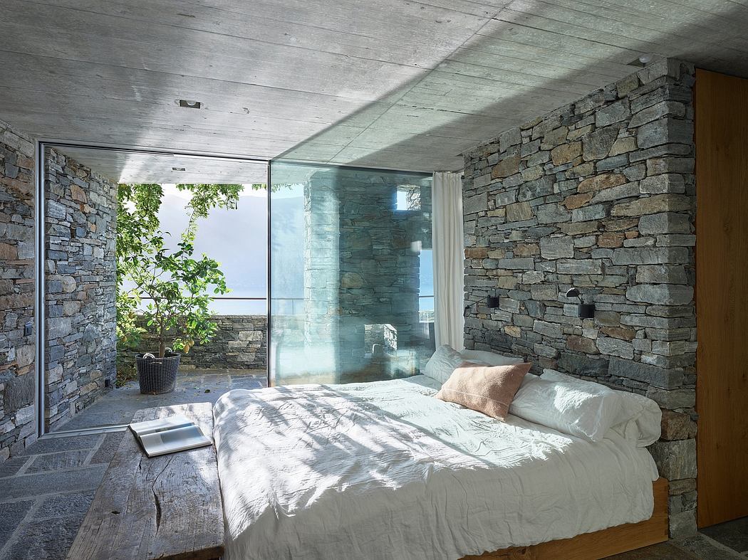 Modern bedroom with stone walls, glass corner, and sea view.