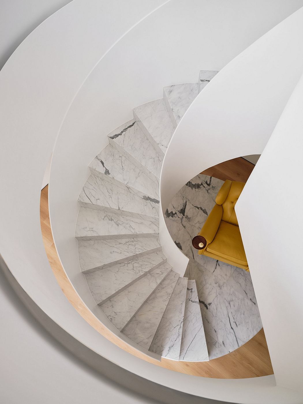 Spiral staircase with gray marble steps and a curved wood railing in a modern interior.