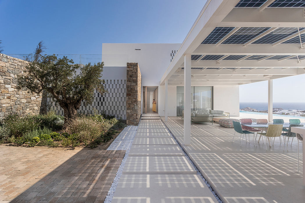 Modern patio with shaded area, chairs, and sea view.