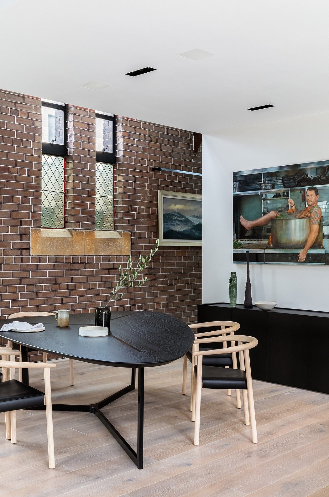A modern dining area with a sleek black table, wood chairs, and a brick feature wall.