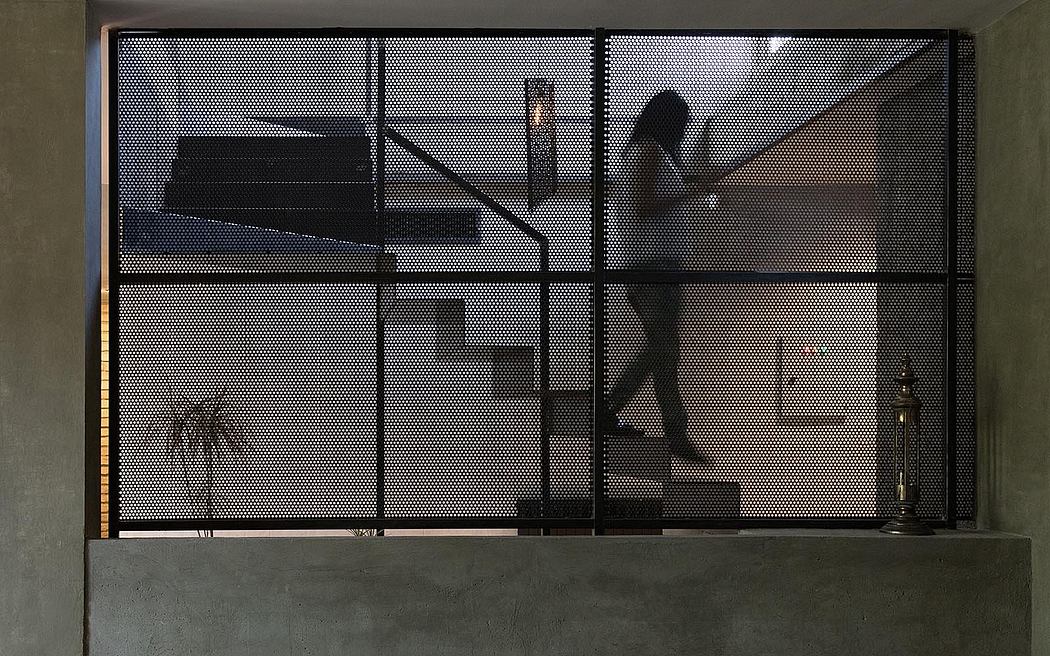 Person ascending a modern staircase behind a perforated metal screen.