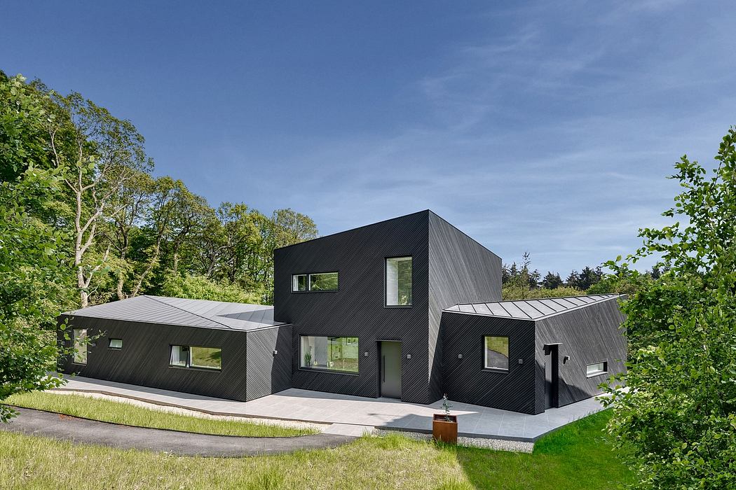A modern, angular black structure with large windows amidst lush green foliage.
