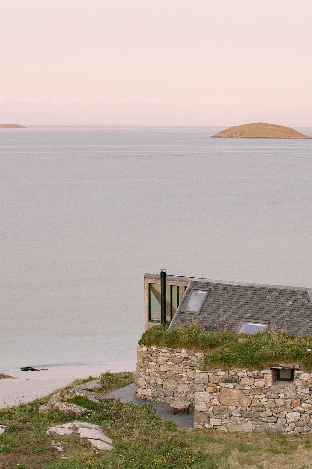 Stone cottage by the sea with grass roof and distant islands.