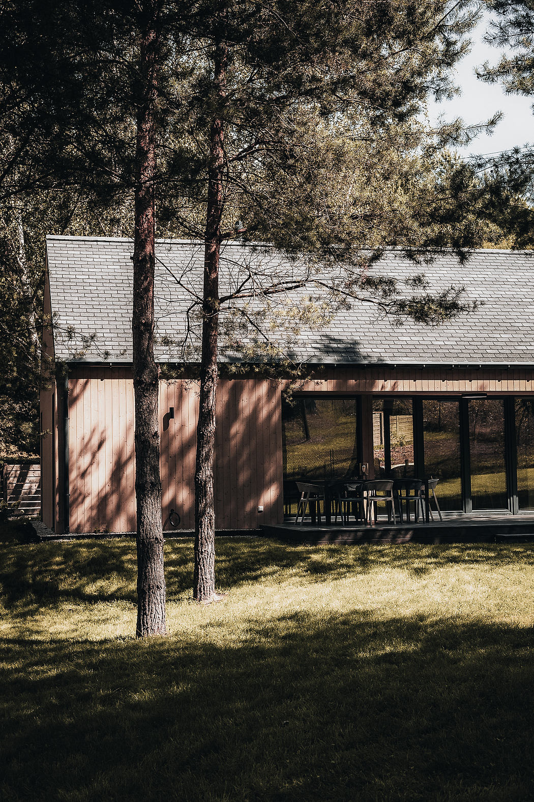 A rustic cabin nestled among pine trees, with a covered porch and brick accents.