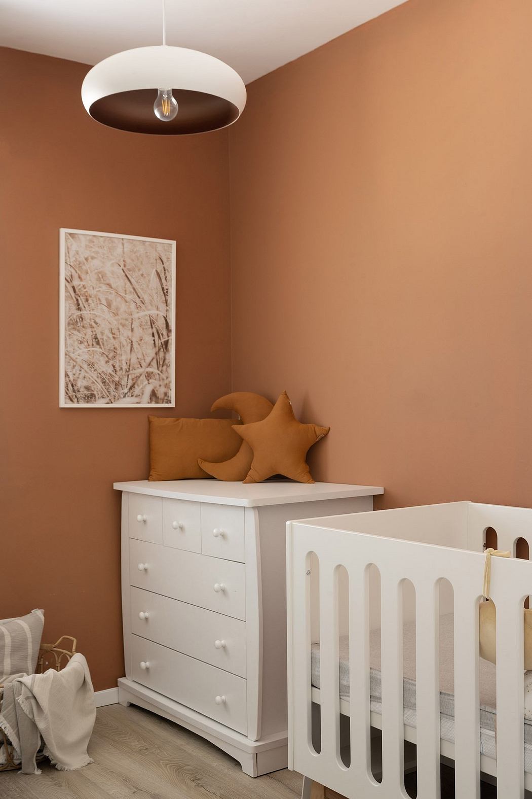 Cozy nursery with terracotta walls, white crib, dresser, and star