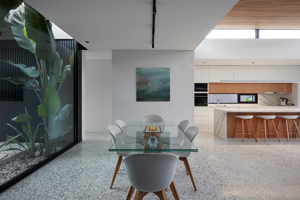 Modern dining room with glass table, indoor plants, and adjacent kitchen.