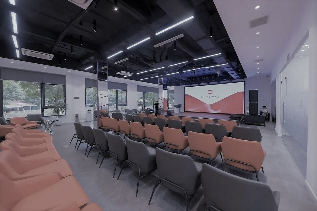 A modern, sleek conference room with tiered seating, lighting fixtures, and a large projection screen.