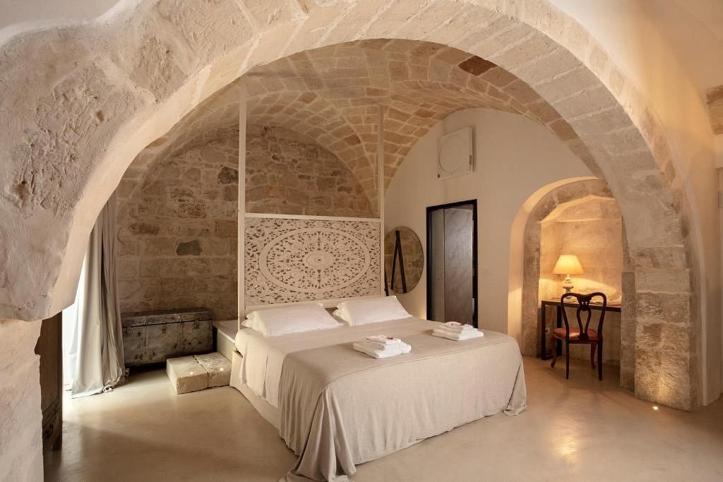 Rustic stone arched alcove with decorative wooden headboard, cozy bedroom setting.