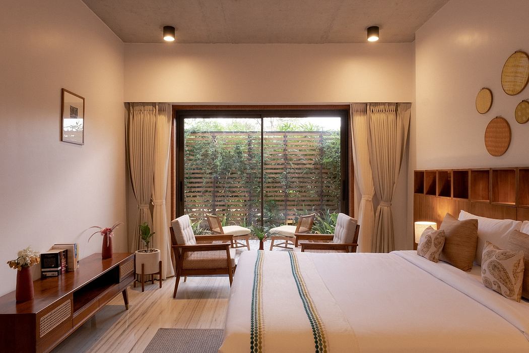 A cozy bedroom with warm lighting, rattan furniture, and a view of a lush outdoor area.