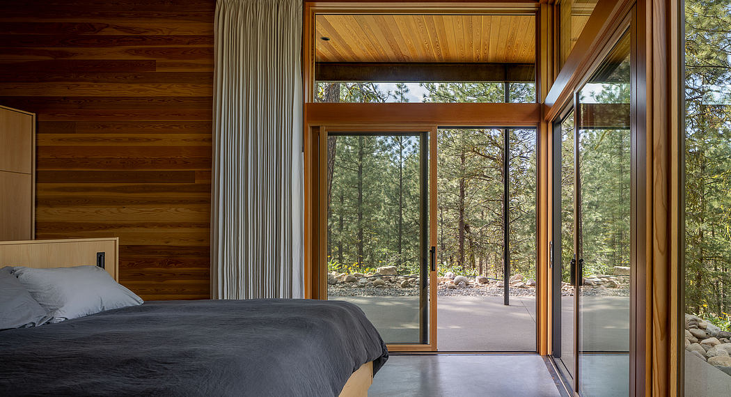 Modern bedroom with large windows overlooking a forest.