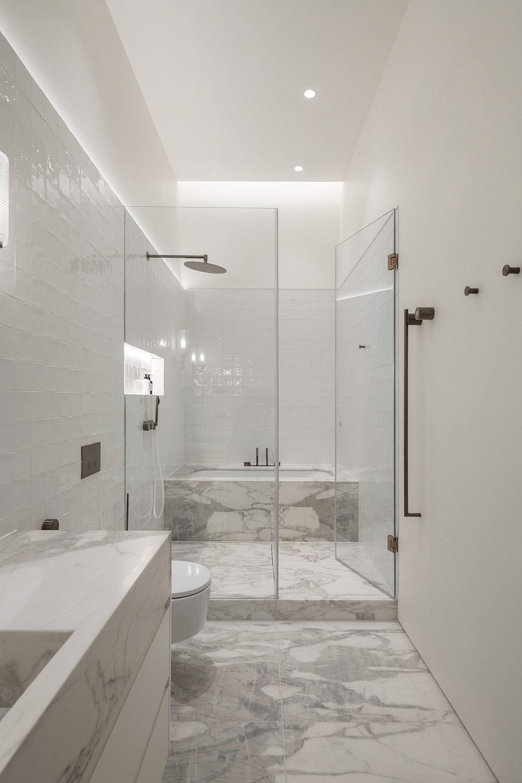 Minimalist white marble bathroom with glass shower enclosure.