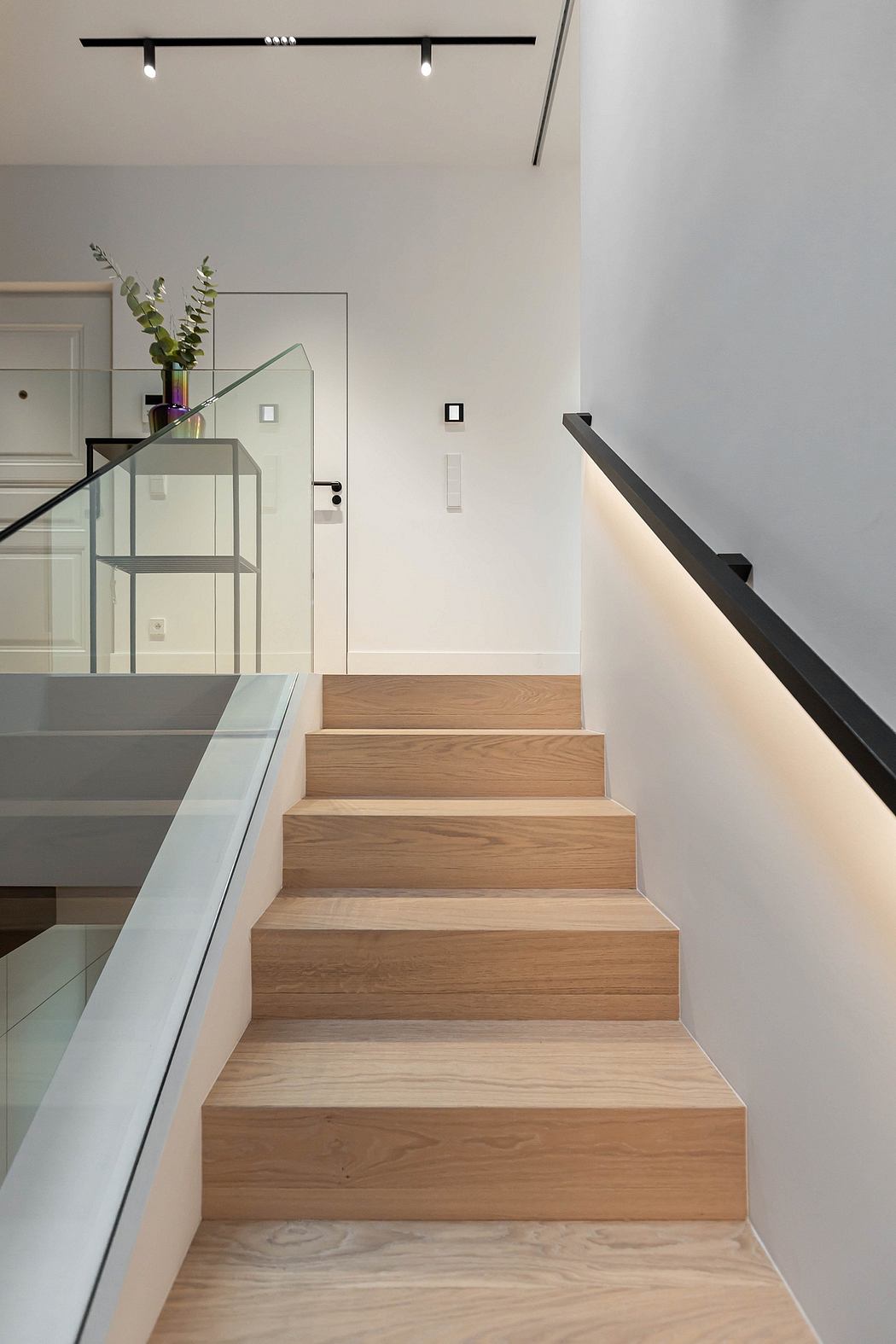 Modern staircase with wooden steps, glass balustrade, and LED lighting.