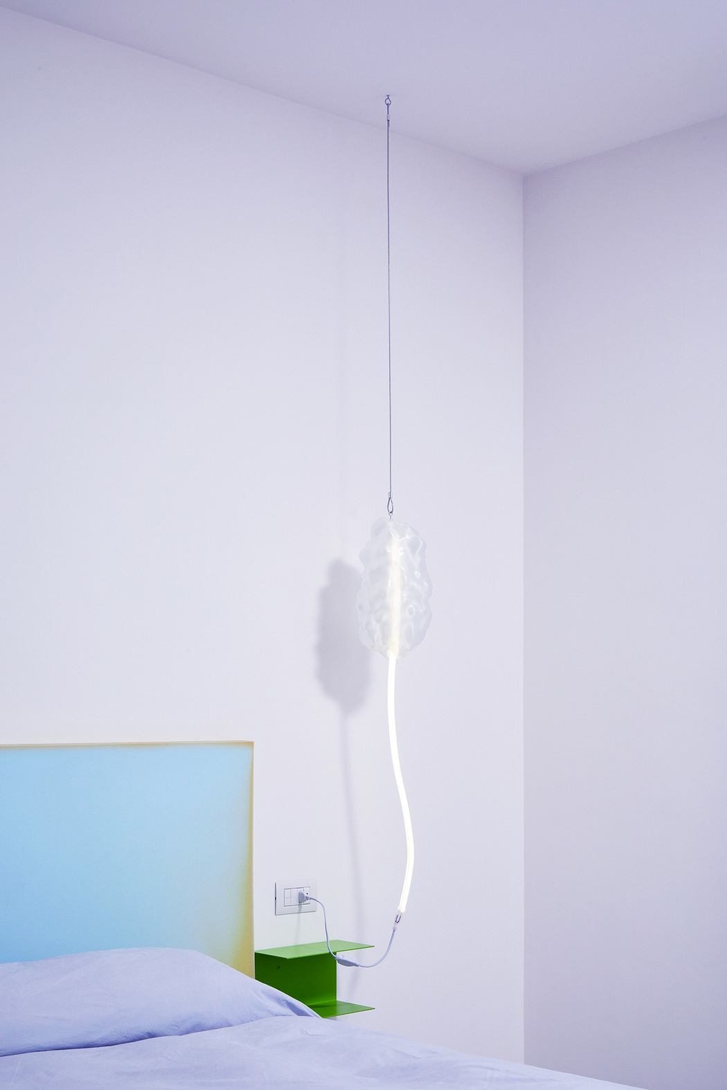 Minimalist bedroom interior with suspended lighting fixture and colorful accents.