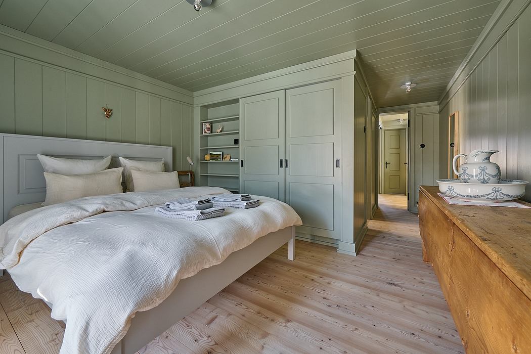A cozy bedroom with wooden floors, pastel green walls, and classic furniture.