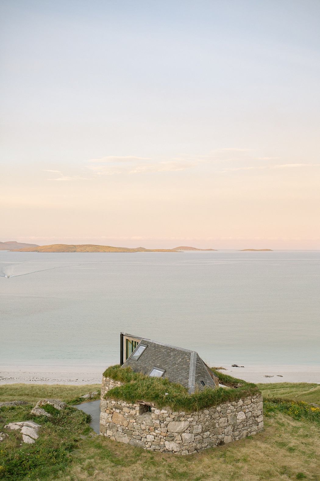 Coastal stone house with grass roof overlooking the sea.