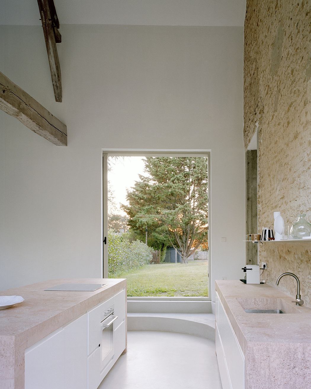 A minimalist bathroom with a stone wall, white cabinets, and a large window overlooking